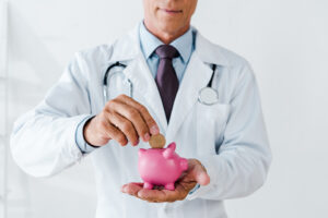 what is cancer costing you - physician with piggy bank dropping coin into it